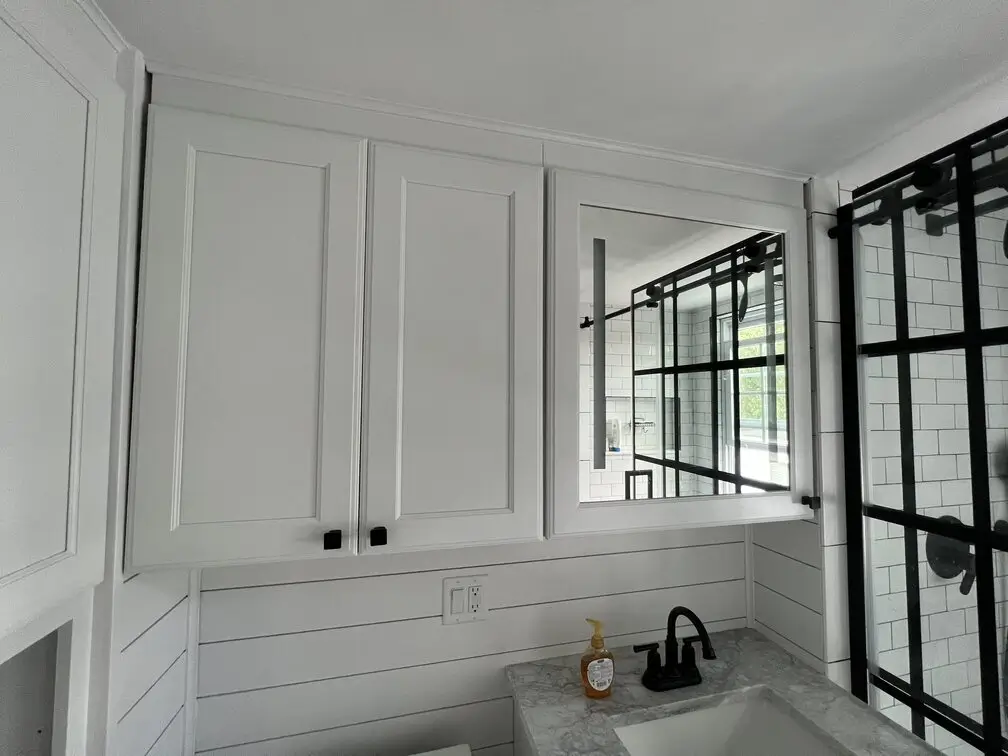Custom mirrored medicine cabinet above marble vanity with black fixtures in a modern Jamaica Plain bathroom.